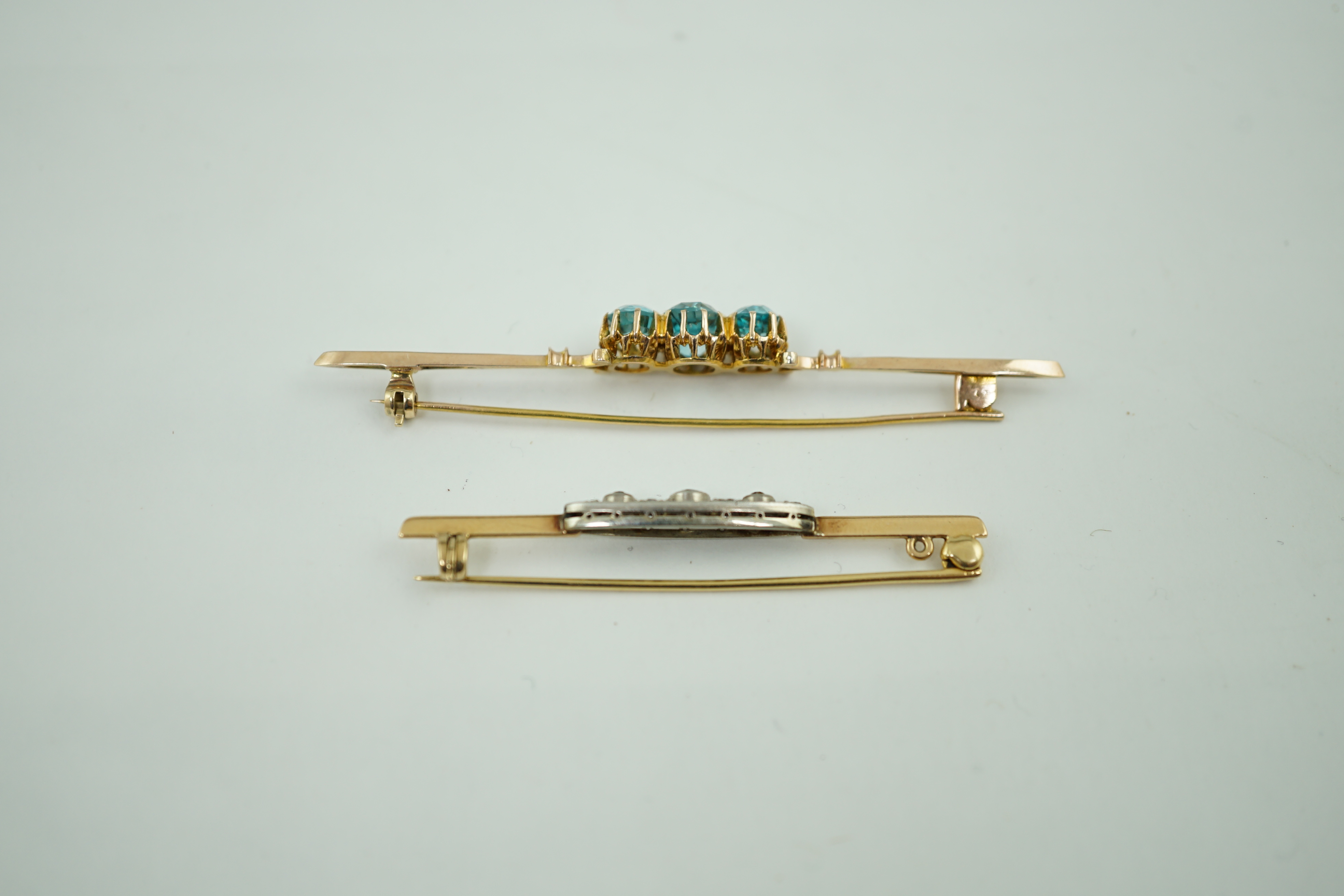 A 1920's yellow metal and millegrain diamond cluster set bar brooch, 56mm, together with a yellow metal and three stone blue zircon set bar brooch